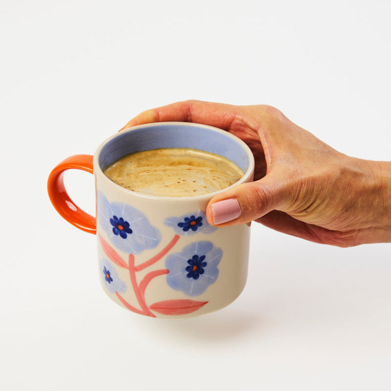 Hand holding a floral-patterned mug with a white background