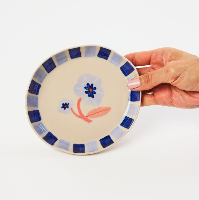 Hand holding a decorative ceramic plate with floral design on a white background