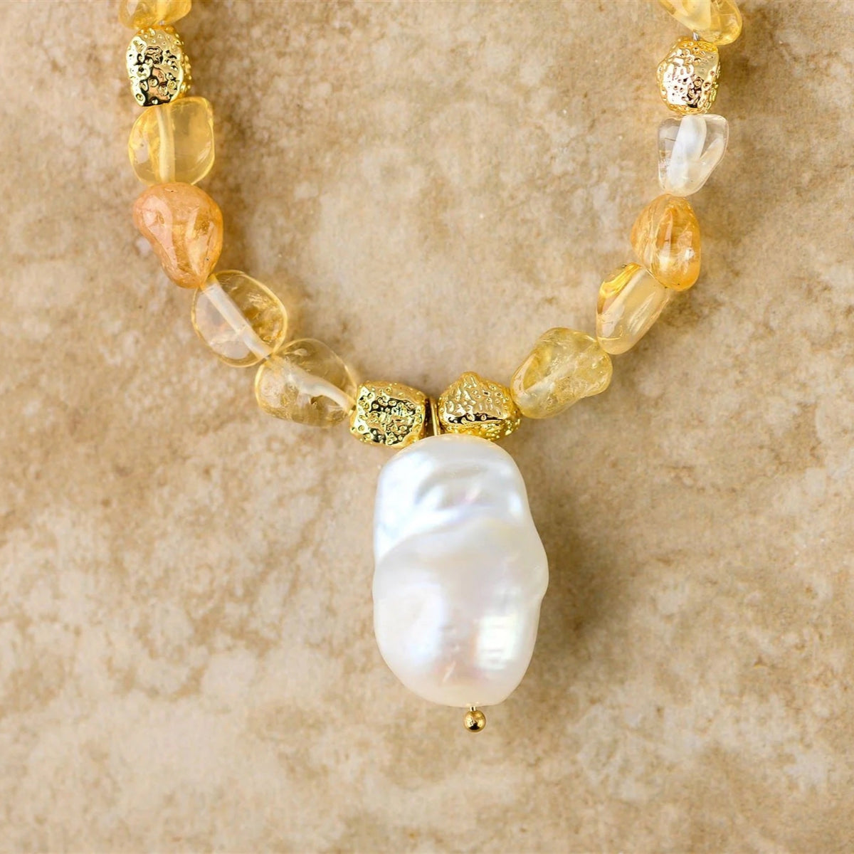 Necklace with gold and yellow beads and a large white pearl on a beige background